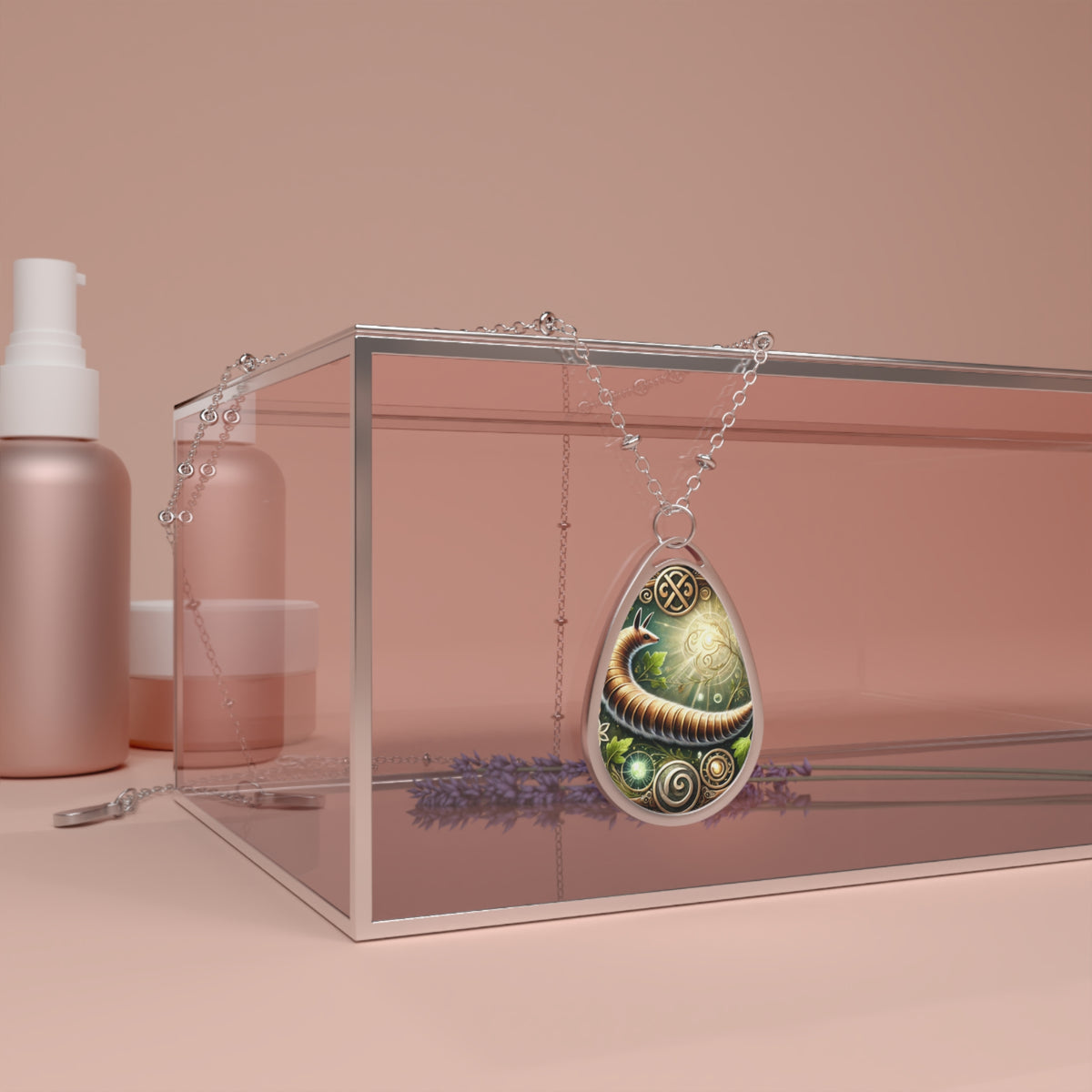 A luxurious display of the Inchworm spirit animal necklace draped over a modern glass box, surrounded by soft pink skincare bottles and sprigs of lavender. The teardrop pendant features an ornate inchworm design, blending earthy greens and golden swirls. The composition exudes sophistication and spiritual symbolism.