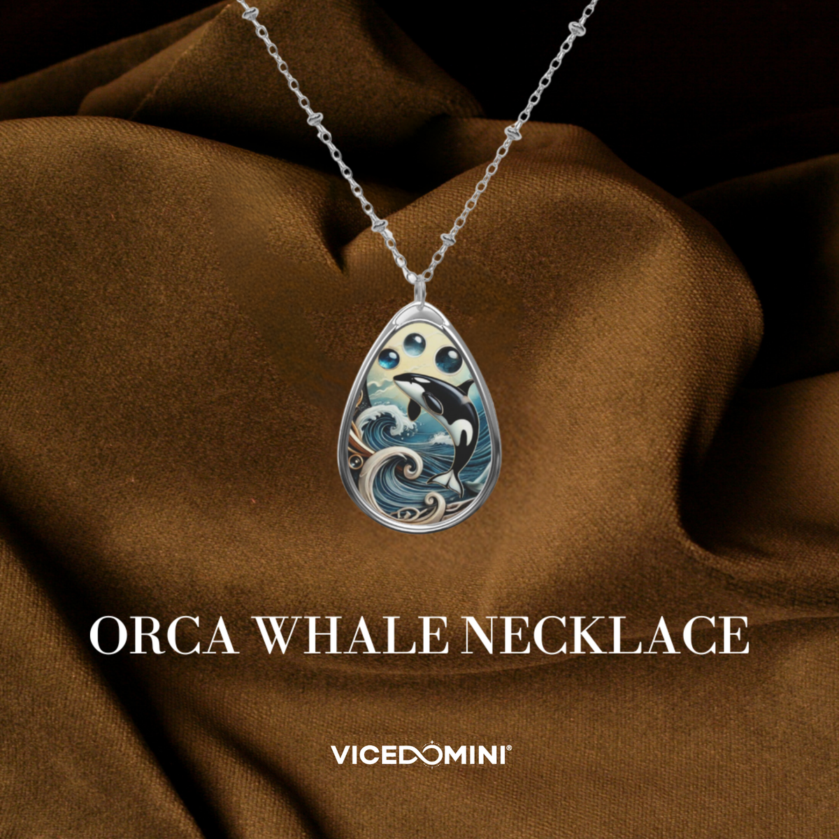 Silver teardrop pendant necklace featuring an orca whale design with blue, white, and black details, displayed on draped brown fabric with the text 'ORCA WHALE NECKLACE' and 'VICEDOMINI'.
