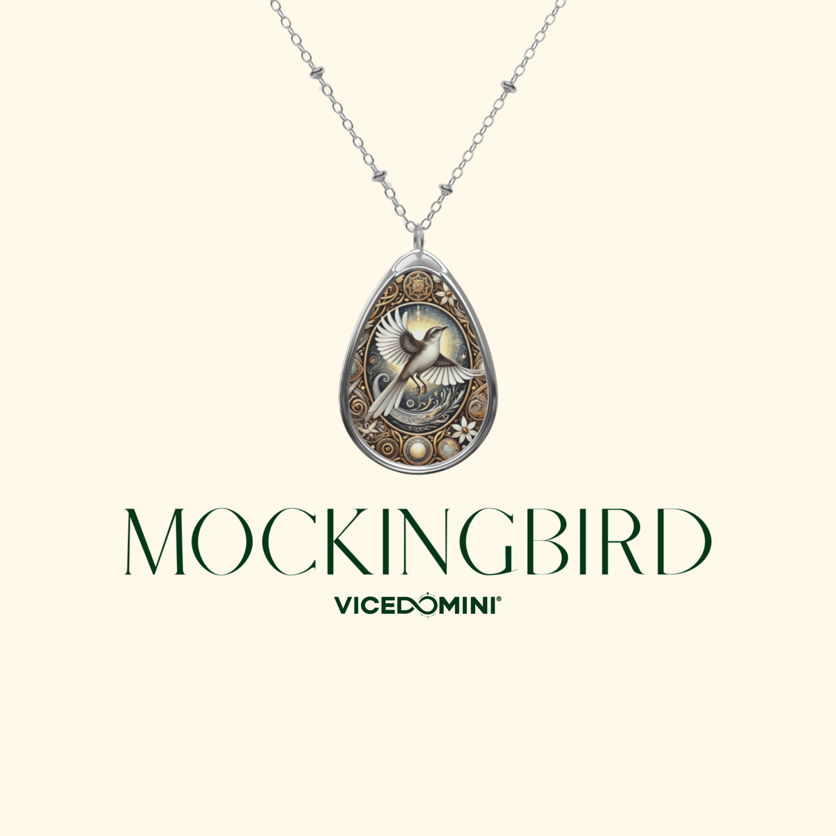 A silver teardrop pendant necklace featuring an engraved bird design, shown against a light cream background with the text 'MOCKINGBIRD' and 'VICEDOMINI' below.