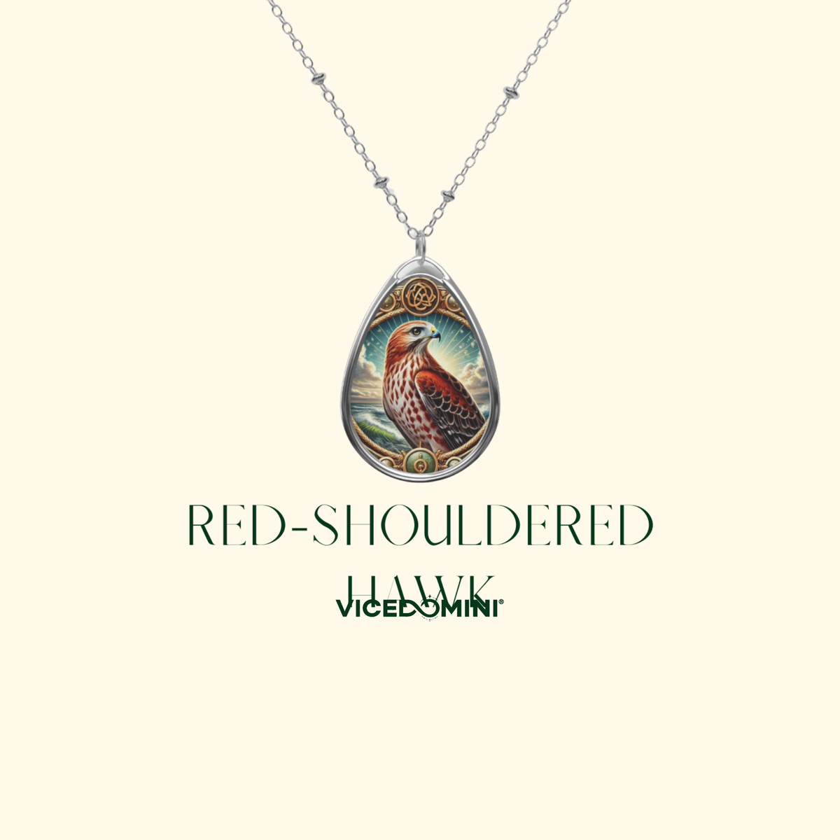 A silver teardrop pendant necklace featuring a detailed illustration of a red-shouldered hawk, displayed on a cream background with the text 'RED-SHOULDERED HAWK vicedomin' below it.